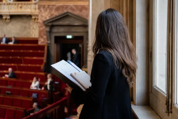 Conseiller parlementaire anonyme avec dossier dans un couloir lumineux de l’Assemblée nationale, sièges rouges flous en arrière-plan
