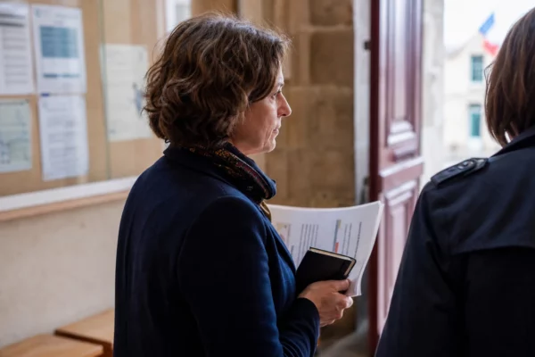 Portrait photojournalistique d’un élu local anonyme dans une mairie, carnet et dossier à la main, lumière naturelle.