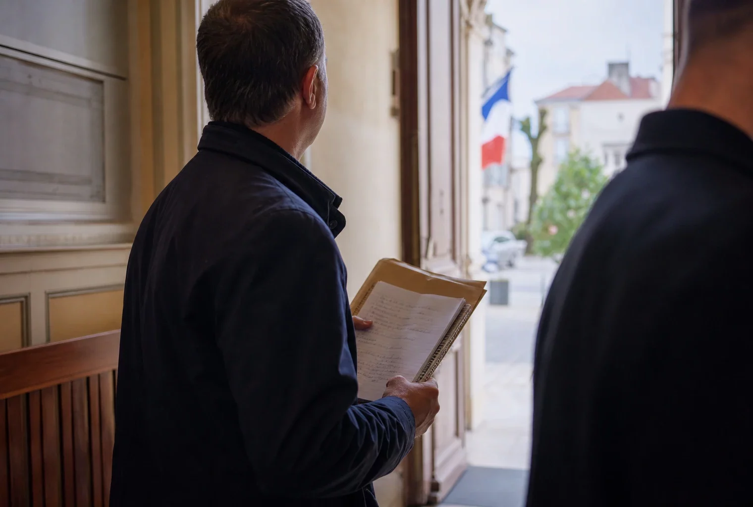 Élu local anonyme tenant un dossier dans un hall de mairie, sur fond de rue française lumineuse.