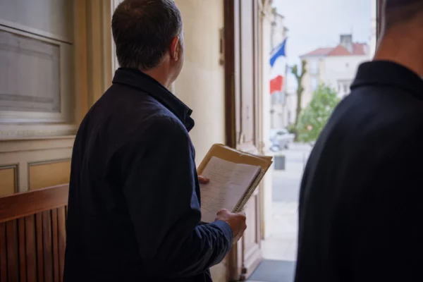 Élu local anonyme tenant un dossier dans un hall de mairie, sur fond de rue française lumineuse.