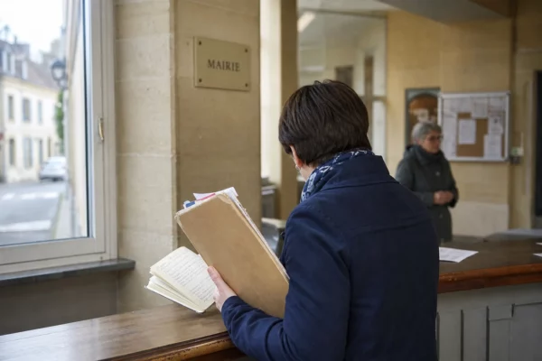 Un collaborateur municipal de dos tient un dossier et un carnet dans une mairie française lumineuse.