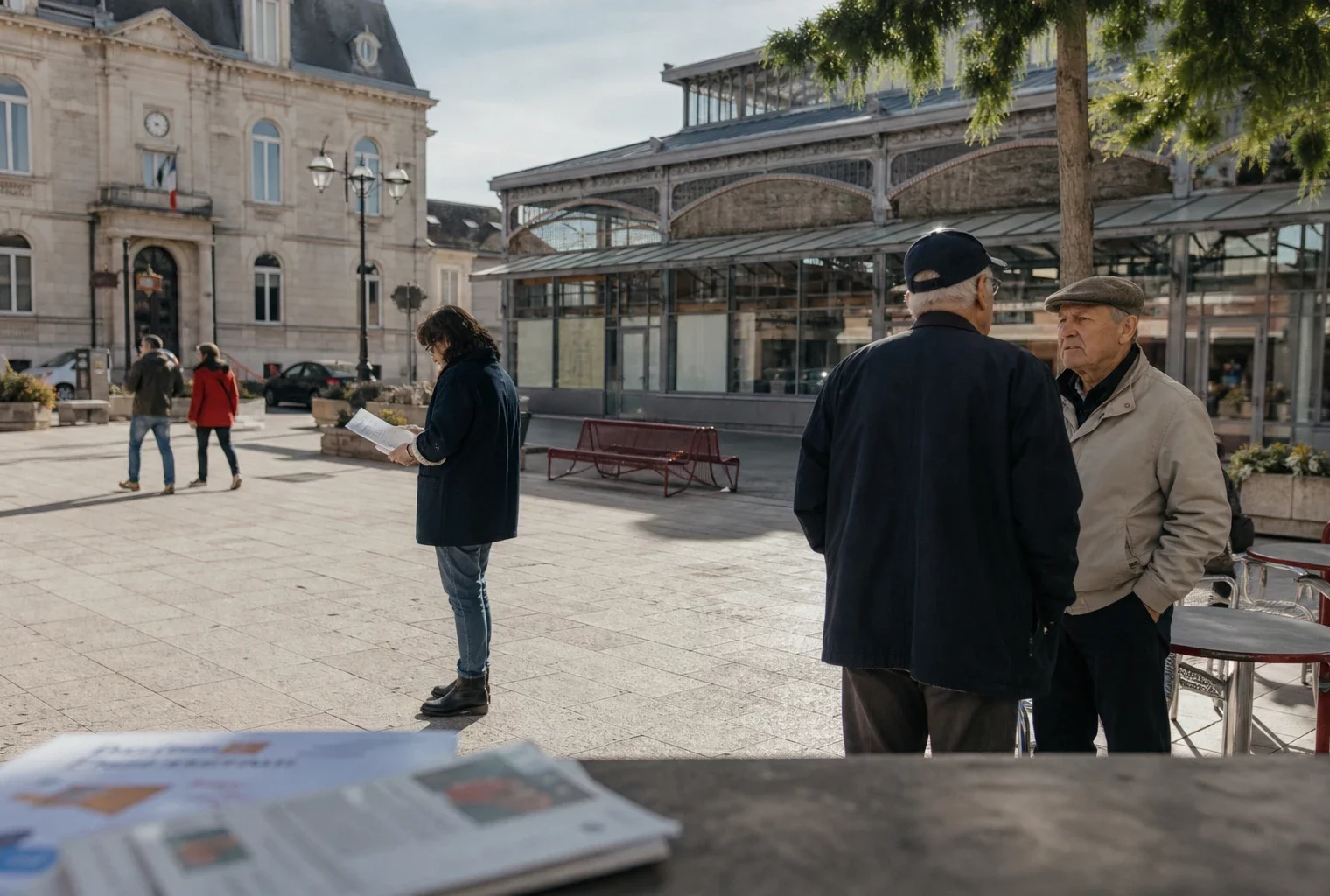 Habitants anonymes sur une place de ville moyenne française, près de la mairie, en discussion calme sous la lumière du jour.