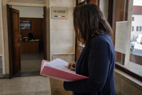 Collaborateur de mairie de dos, dossier à la main, dans un couloir lumineux avec rue française en arrière-plan.