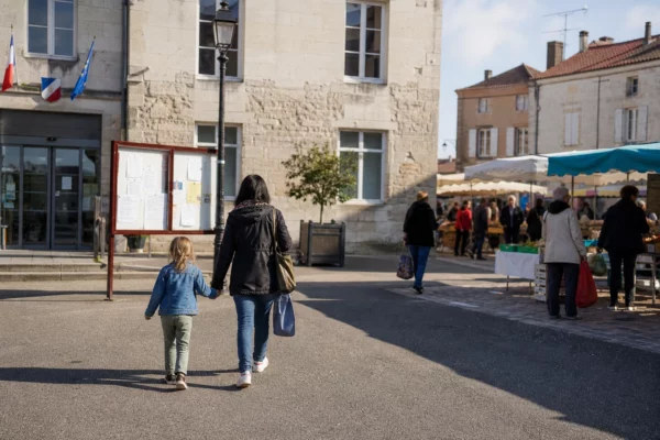 Scène de rue dans une ville française, près d’un bâtiment public, avec des habitants anonymes en activité normale.