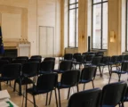 Salle de presse vide au Quai d’Orsay, baignée de lumière naturelle, avec podium et micros devant des fauteuils inoccupés.