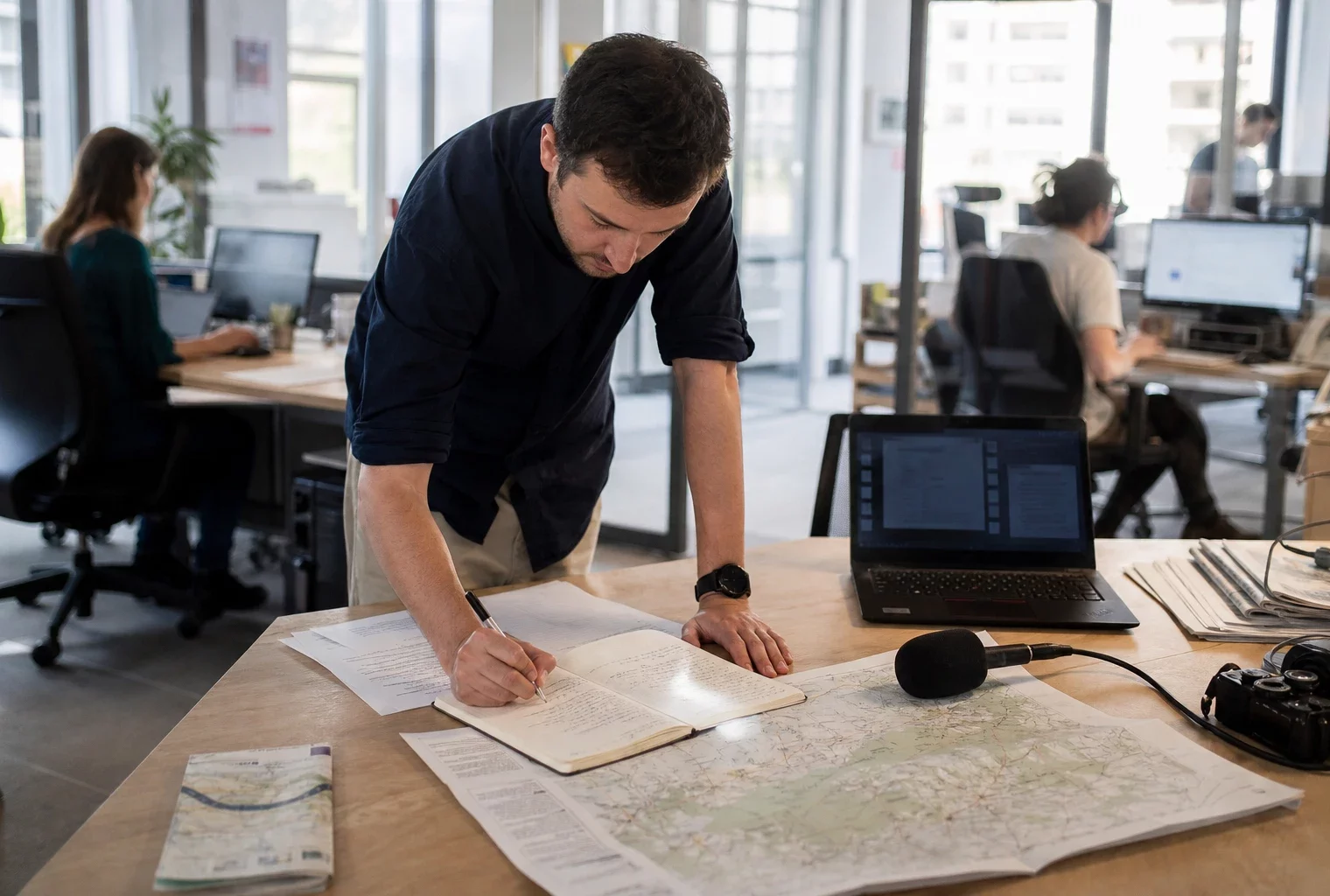 Journaliste en rédaction locale préparant un sujet sur la canicule avec carnet, micro et carte papier floue