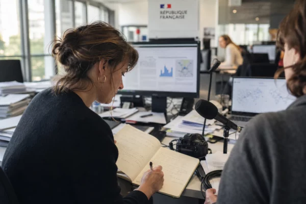 Journalistes en rédaction autour d’écrans flous et de documents, sur un sujet de canicule à Paris.