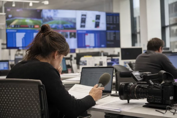Dans une rédaction française, un journaliste prépare un sujet sur la Coupe du monde 2026 devant micros, caméras et écrans flous.