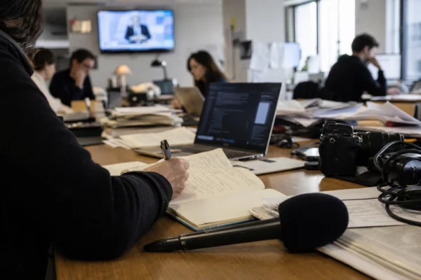 Rédaction française en pleine enquête politique, journaliste prenant des notes près d’un micro et d’écrans flous.