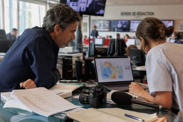 Une rédaction française prépare un sujet sur la chaleur du Mondial 2026, avec écrans flous et journaliste au travail.