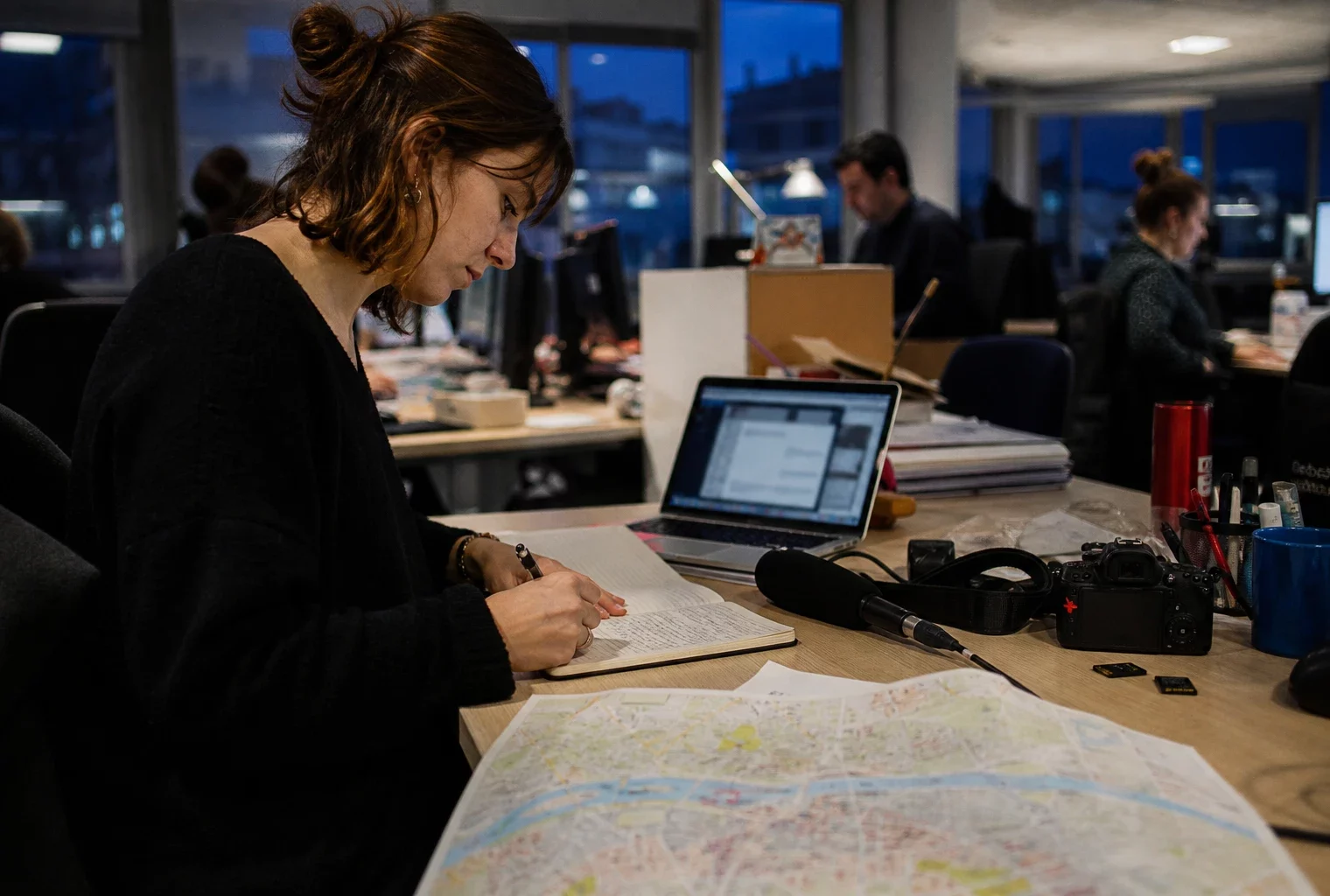 Journaliste préparant un sujet politique dans une rédaction française, avec carnet, micro et écran flou