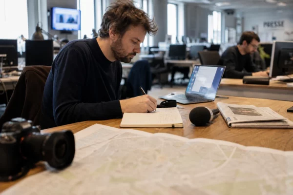 Journaliste en rédaction préparant un sujet politique avec carnet, micro sans logo et carte papier floue.