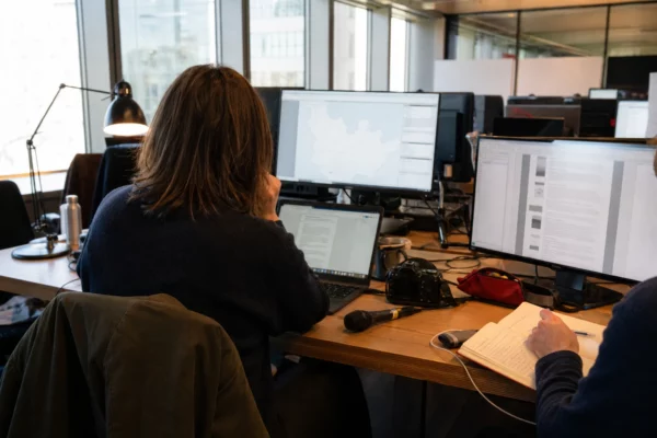 Une rédaction française prépare un sujet sur la protection de l’enfance, avec écrans flous, carnet et micro sans logo.