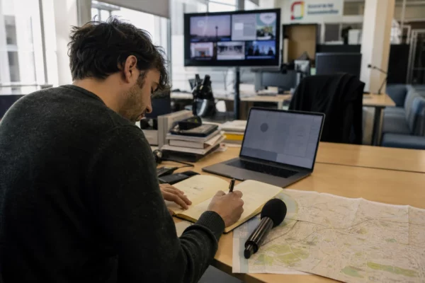Journaliste en rédaction préparant un sujet sur Carcassonne avec carnet, micro sans logo et carte floue.