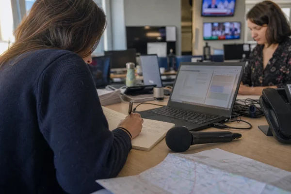 Journaliste en rédaction préparant un sujet territorial avec carnet, micro et carte papier floue.