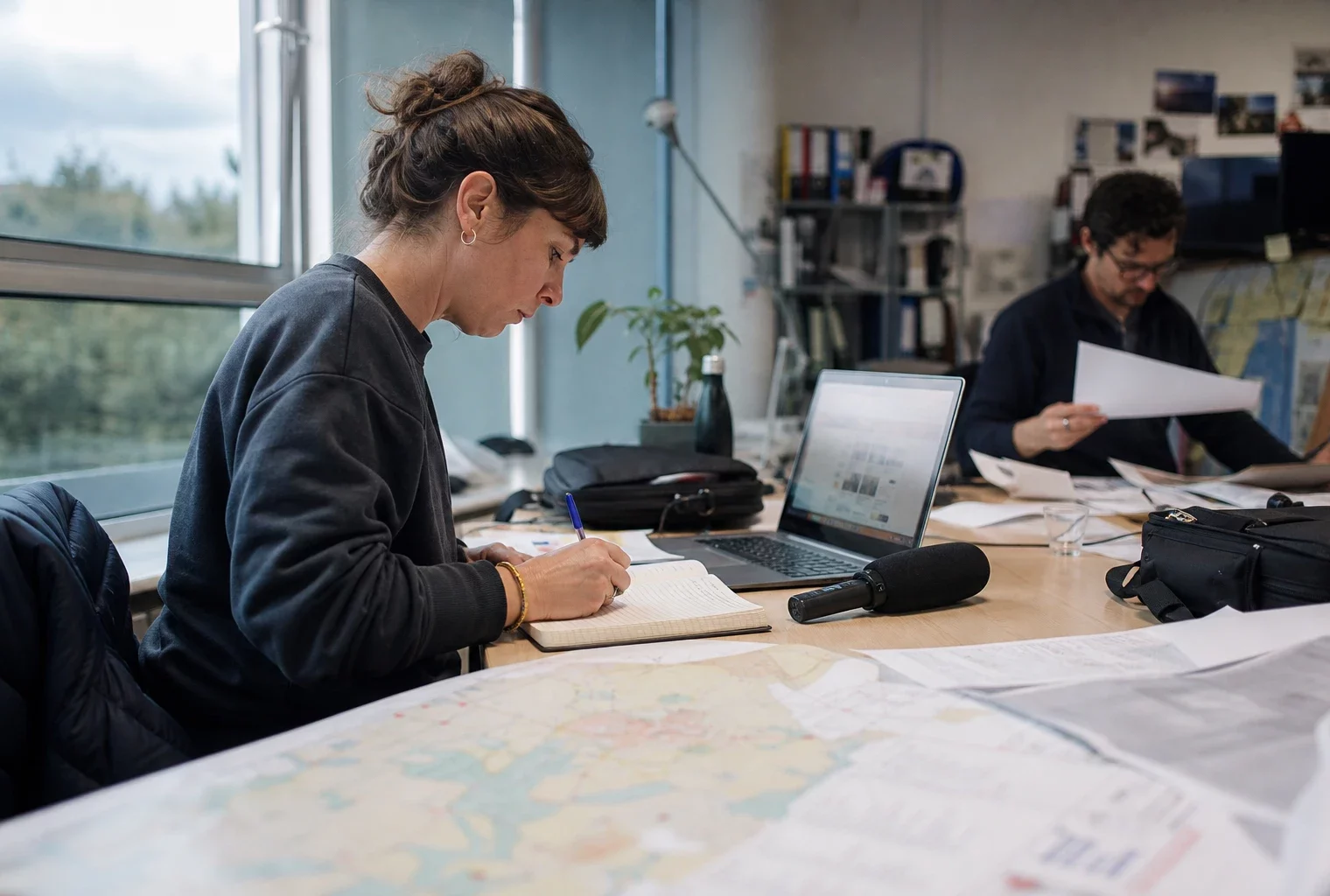 Journaliste en rédaction locale préparant un sujet politique avec carnet, micro et carte papier floue