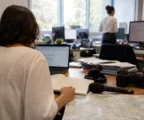 Journaliste en rédaction locale préparant un sujet territorial, avec carnet, micro sans logo et écrans flous.