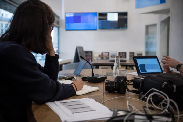 Réunion de rédaction dans un newsroom parisien avec journalistes, micros, caméra et écrans flous.