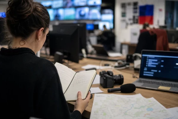 Journaliste en rédaction préparant un sujet politique avec carnet, micro sans logo et carte floue sur le bureau.