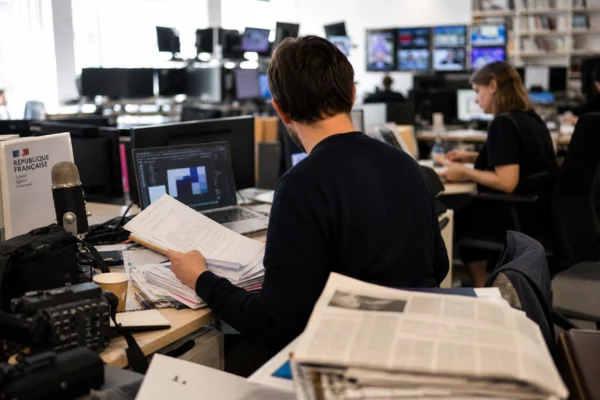 Journaliste dans une rédaction parisienne avec écrans flous et documents européens sur le bureau