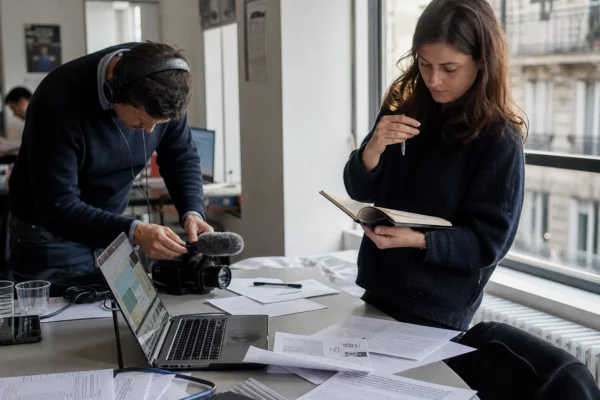 Journalistes en rédaction préparant un sujet politique, avec micro, carnet et écran d’ordinateur flouté.