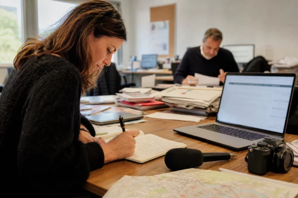 Journaliste en rédaction préparant un sujet sur la justice et la protection des enfants, carnet et micro sur la table