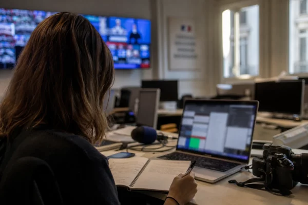 Journaliste en rédaction préparant un sujet sur Ursula von der Leyen, avec micro, caméra et écrans flous