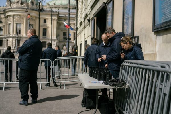 Reportage calme devant un lieu culturel parisien avec du matériel de sécurité et des silhouettes anonymes en journée.