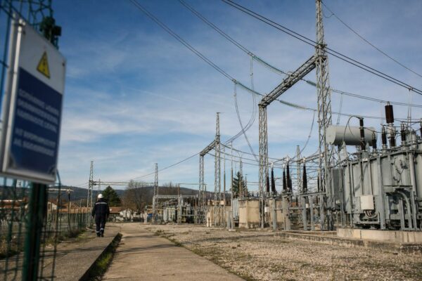 Sous-station électrique française au soleil avec pylônes et lignes à haute tension, un technicien au loin