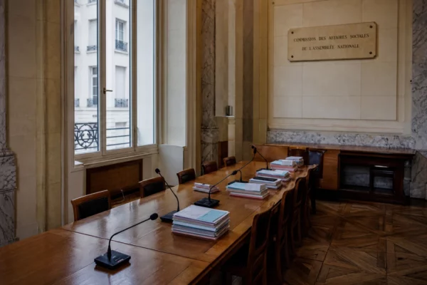 Salle institutionnelle vide avec dossiers de retraite et micros, éclairée par une grande lumière naturelle.