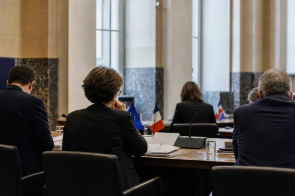 Réunion européenne sobre avec dossiers et petites drapeaux de table, vue de dos en salle institutionnelle claire.