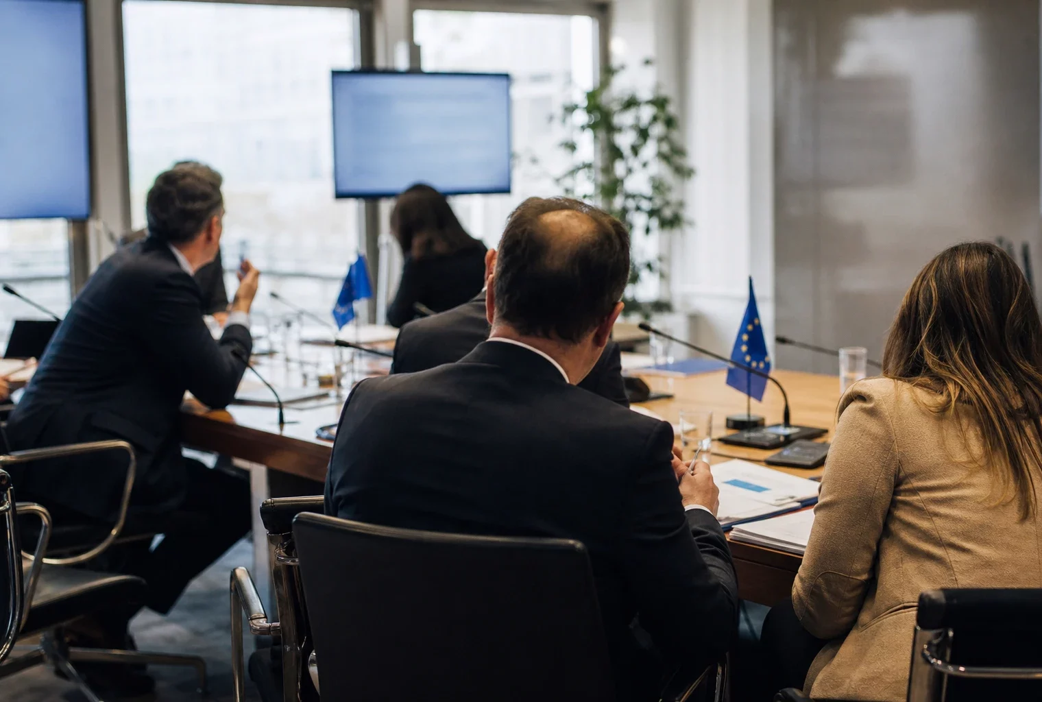 Réunion européenne sobre avec dossiers, micros et drapeaux de table discrets dans une salle institutionnelle lumineuse.