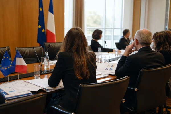 Réunion européenne sobre avec dossiers et drapeaux de table, autour d’une loi sur les violences sexistes et sexuelles