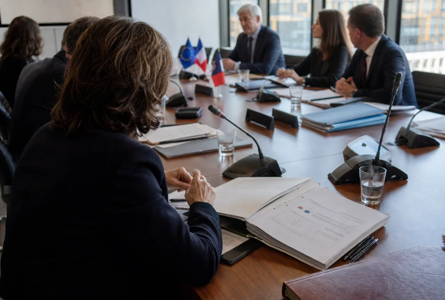 Réunion européenne sobre avec dossiers et micros, autour d’une table institutionnelle, dans une lumière naturelle claire.
