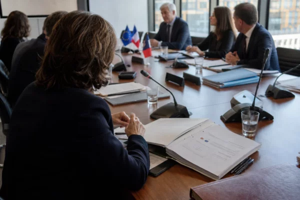 Réunion européenne sobre avec dossiers et micros, autour d’une table institutionnelle, dans une lumière naturelle claire.