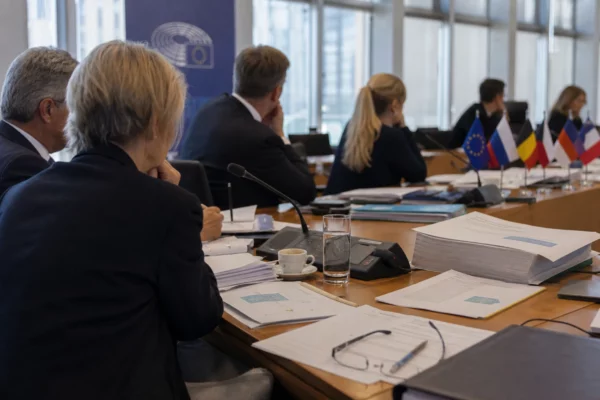 Réunion sobre au Parlement européen avec cinq silhouettes de dos, dossiers ouverts et micros sur la table.