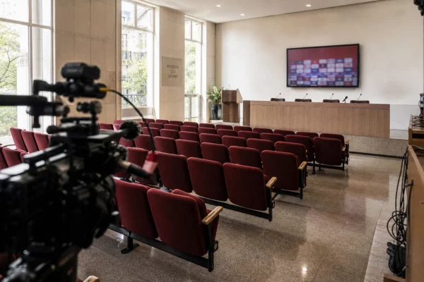 Salle de briefing vide dans un bâtiment sportif français, avec rangées de sièges rouges et podium sous une lumière naturelle claire.