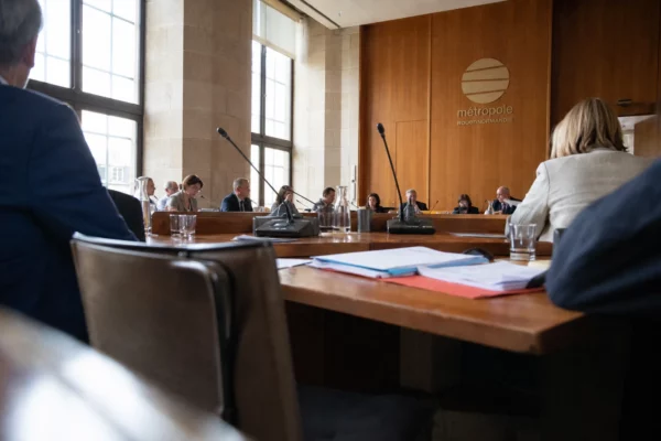 Salle municipale à Rouen avec micros, dossiers et une chaise vide lors d’une séquence politique locale.