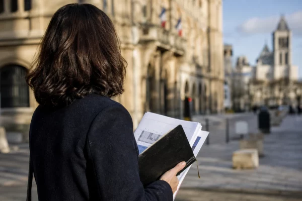 Un élu local anonyme prend des notes près de la mairie de Saint-Denis, avec la basilique floue en arrière-plan.