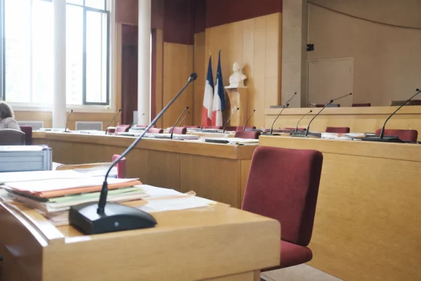 Salle du conseil municipal éclairée naturellement, avec une chaise vide, des micros et des dossiers flous.