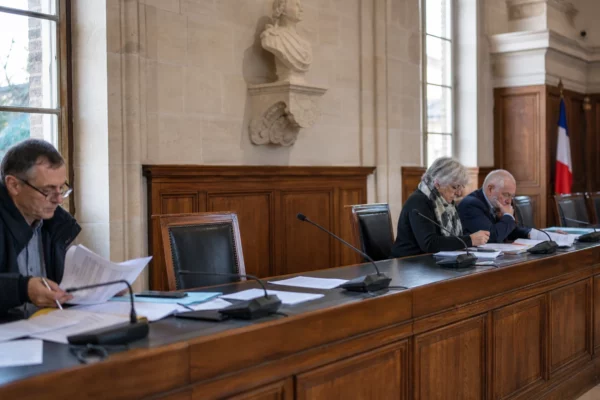 Salle de conseil municipal en lumière naturelle avec chaise vide, micros et dossiers flous sur une longue table.