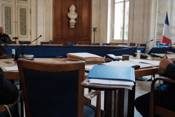Salle du conseil municipal à Nice, avec chaise vide, micros et dossiers sur une longue table éclairée par la lumière du jour.