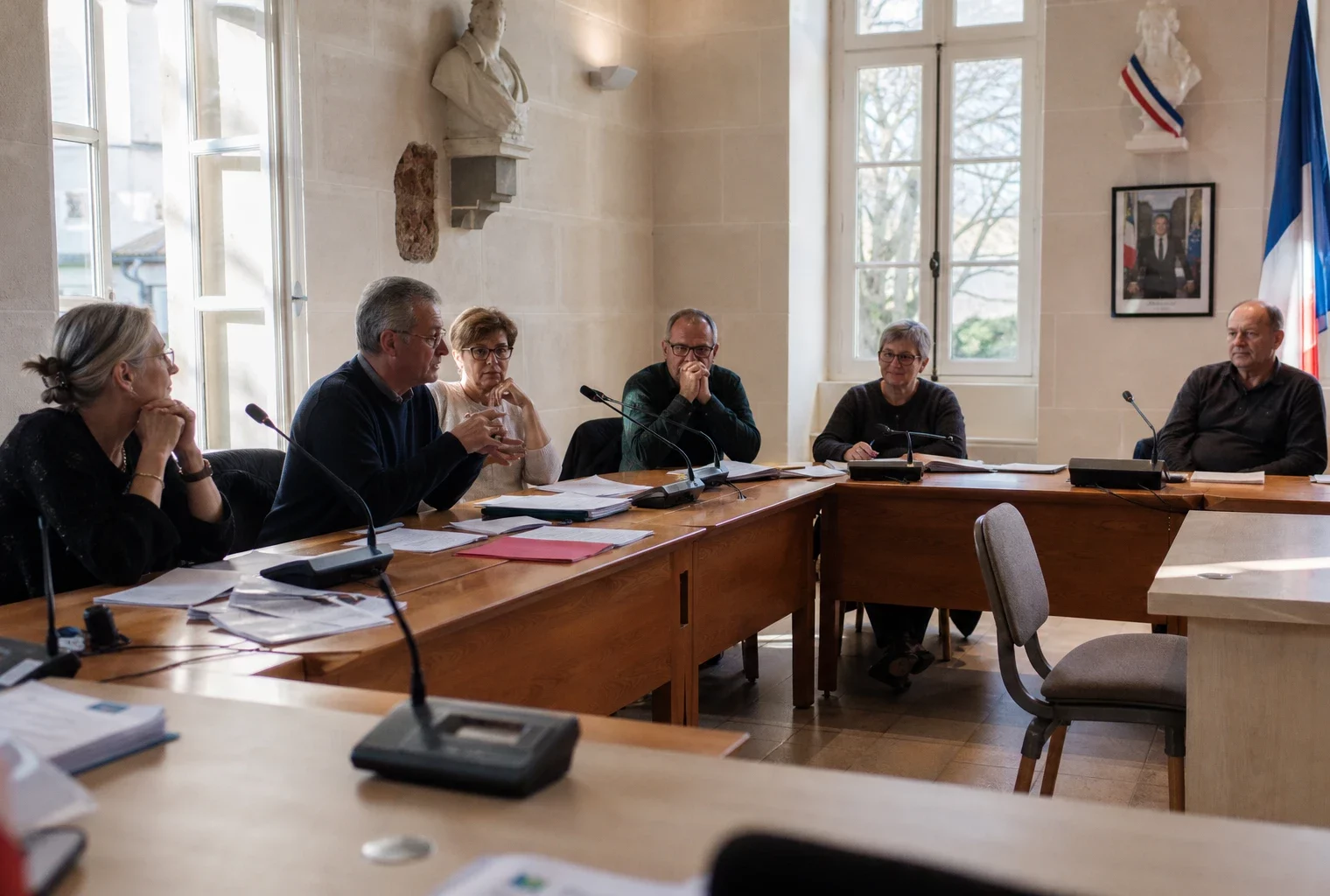 Salle municipale normande avec micros, dossiers et chaise vide lors d’une réunion sur les fonds européens