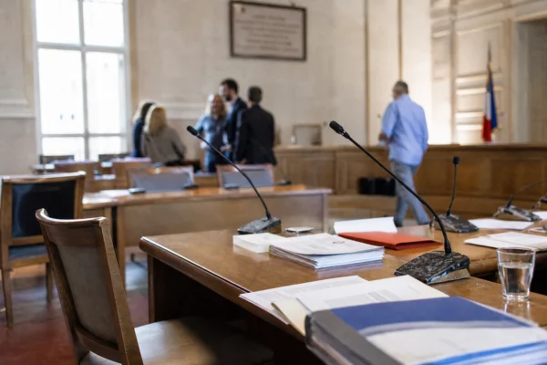 Salle municipale avec micros, dossiers et chaise vide lors d’une réunion sur la protection des enfants