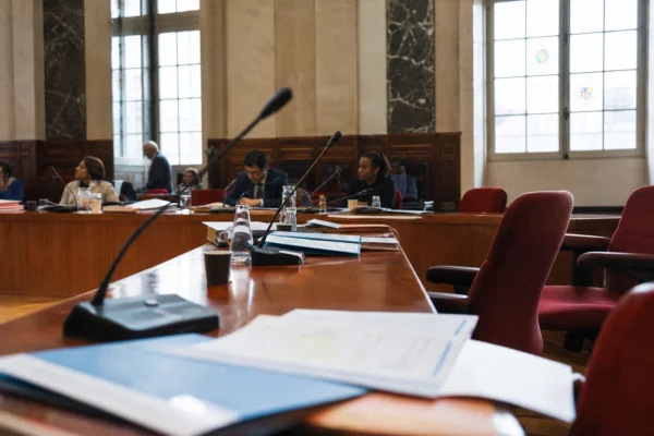 Salle municipale de Saint-Denis avec micros, dossiers et une chaise vide au centre d’une réunion locale.