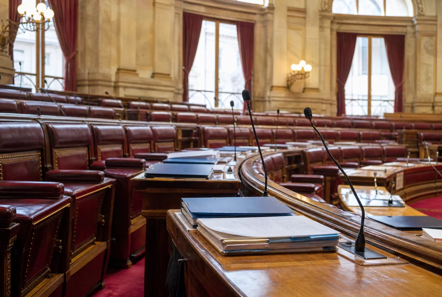 Salle du Sénat vide avec pupitres, dossiers fermés et micros, dans une lumière naturelle claire de reportage.