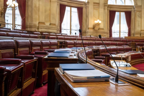 Salle du Sénat vide avec pupitres, dossiers fermés et micros, dans une lumière naturelle claire de reportage.