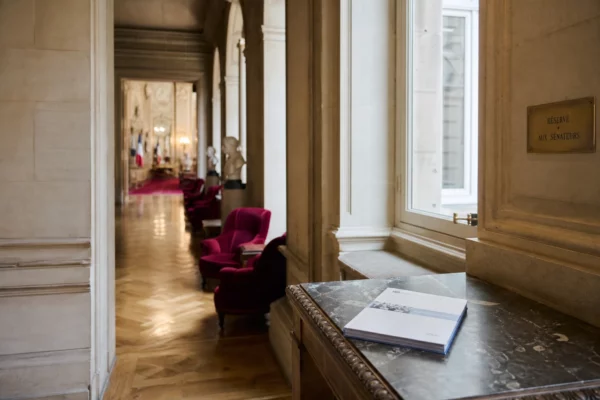 Couloir du Sénat vide avec marbre clair, sièges rouges et dossier législatif posé sur une table.