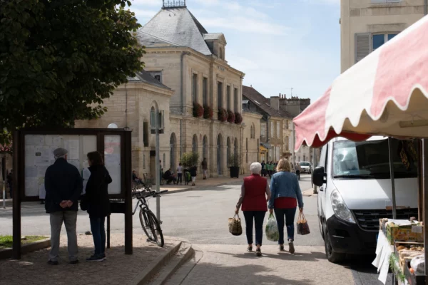 Devant une mairie de petite ville en Côte-d'Or, des habitants traversent une rue calme sous une lumière naturelle.