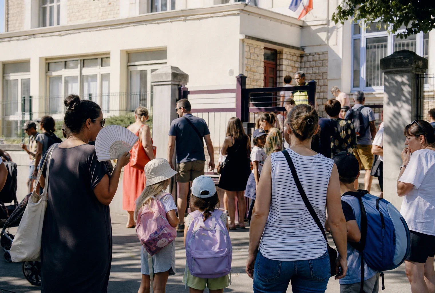 Parents anonymes à la sortie d’une école publique française par forte chaleur, sous une lumière de matin claire.